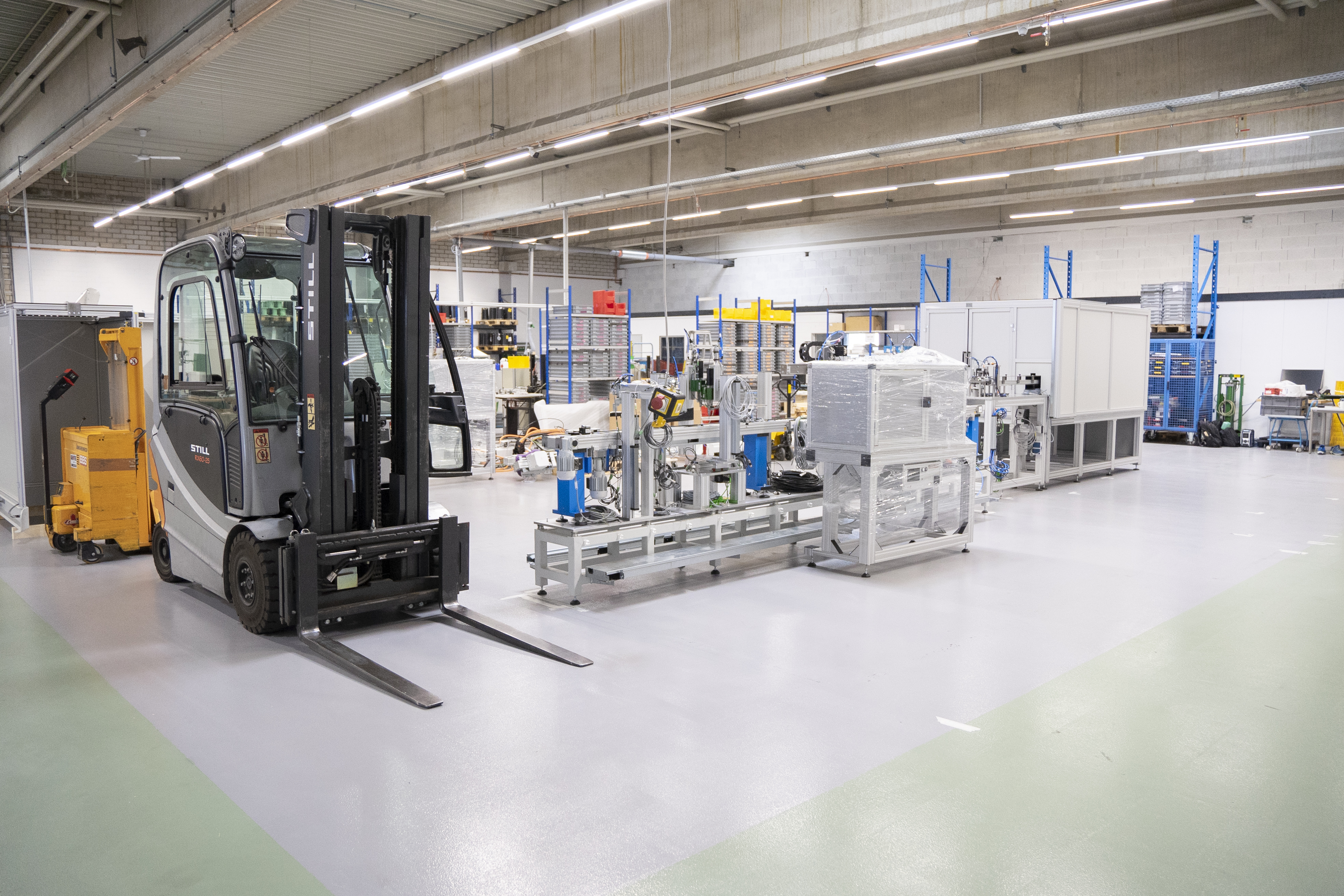 Gabelstapler in der Produktionshalle, daneben stehen die ersten Teile der Maschine