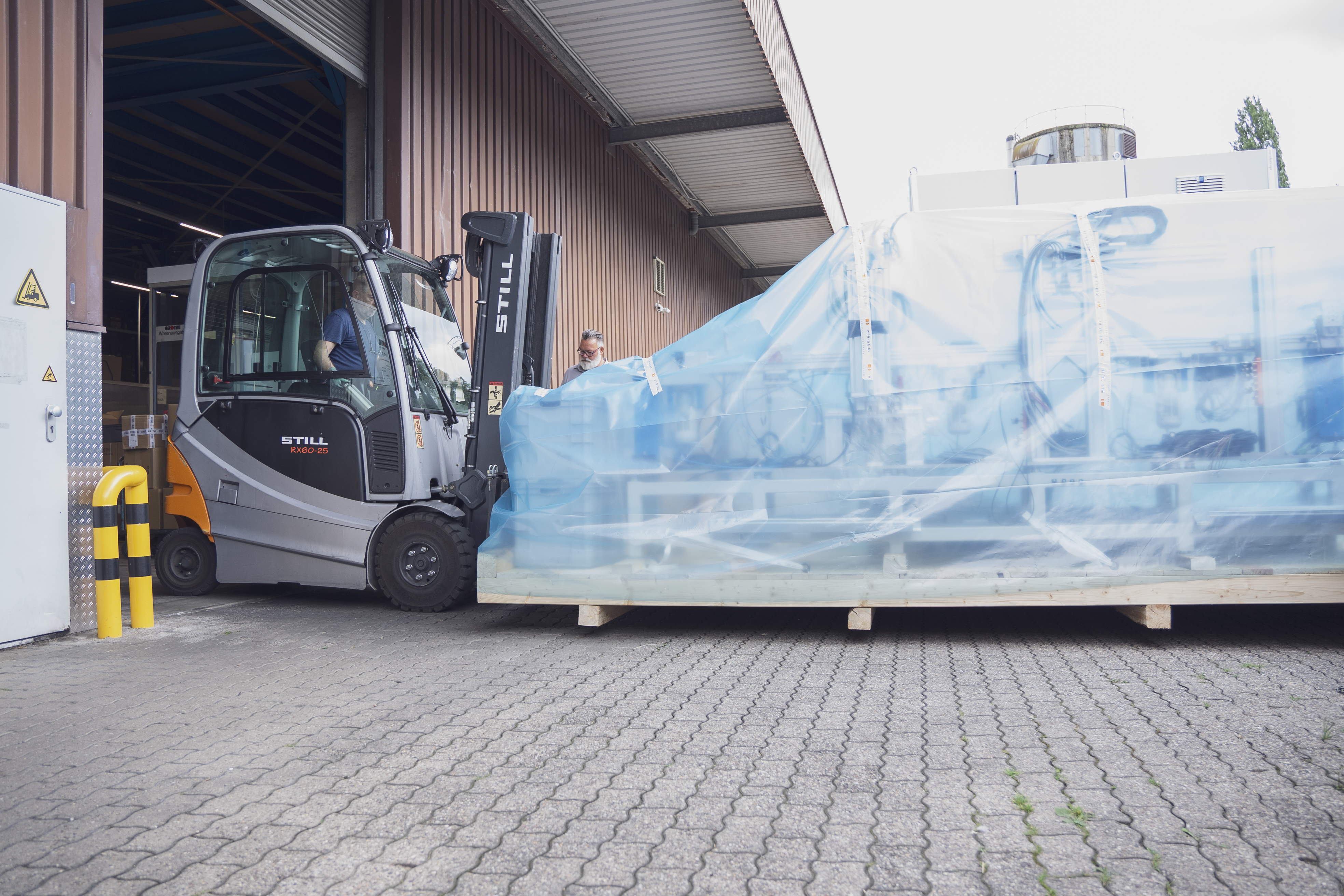 Ein Gabelstapler fährt eine große Palette mit Teilen der Maschine, die mit blauer Plastikfolie geschützt sind, in die Lagerhalle
