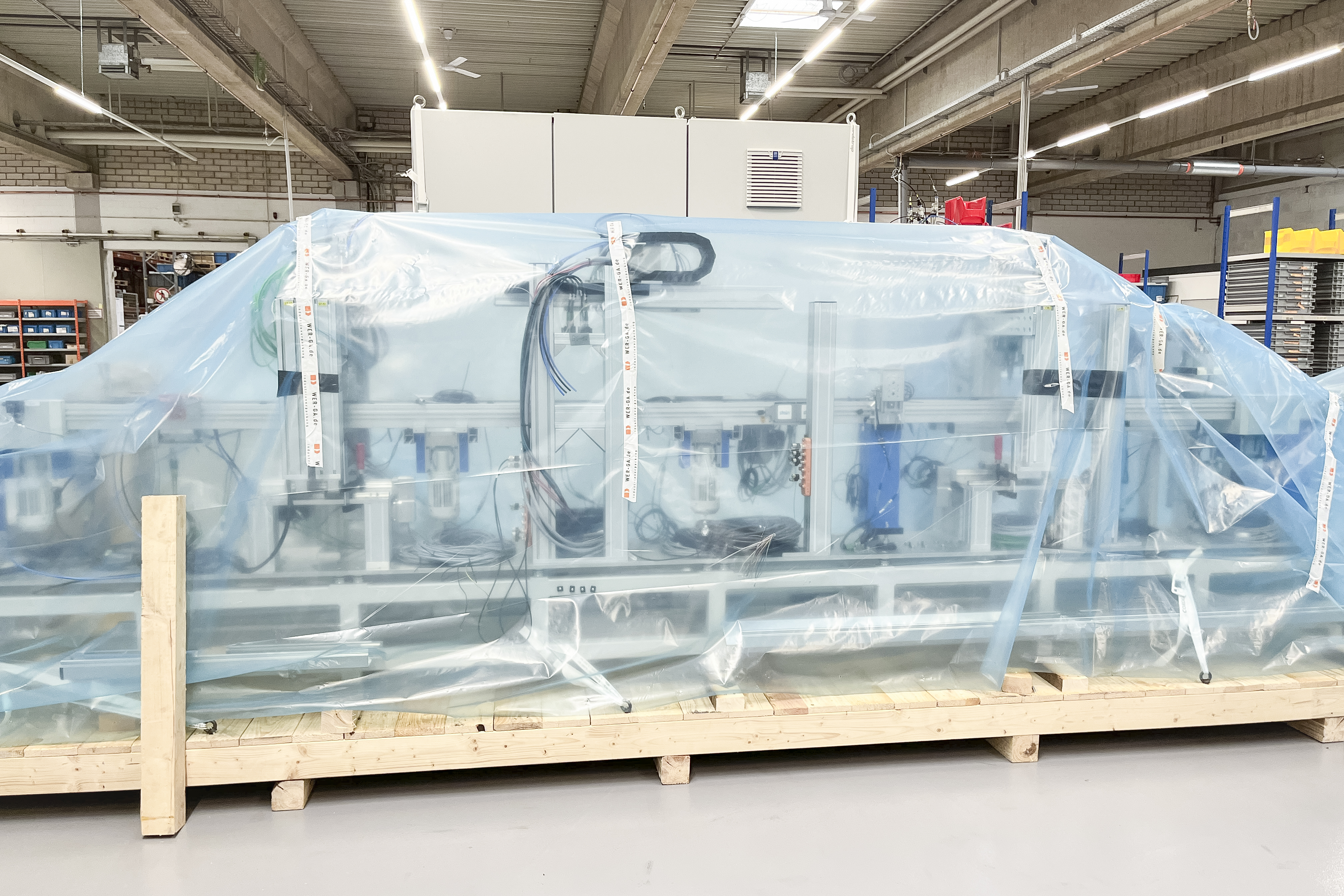 Eine große Palette mit einer Produktionsstraße der Maschine, die mit blauer Plastikfolie abgedeckt ist, steht in der Produktionshalle